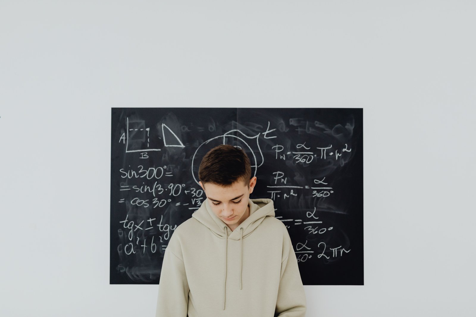 Teenager in a classroom solving mathematics equations on a blackboard, deep in thought.