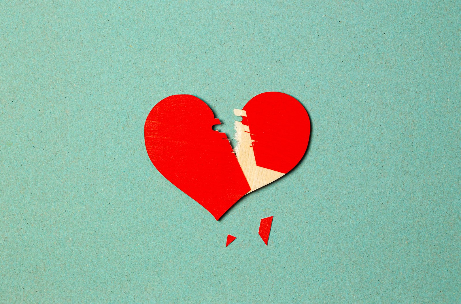 A torn red paper heart on a blue background symbolizes broken love or heartache.
